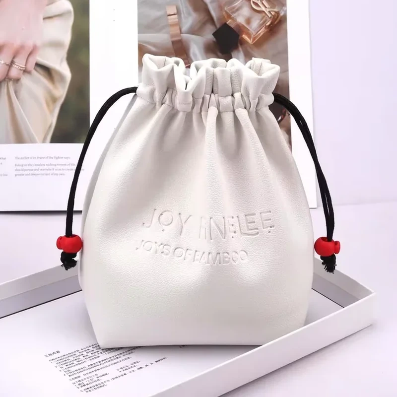 White leather-look drawstring bag with black cords, red beads and a rounded base