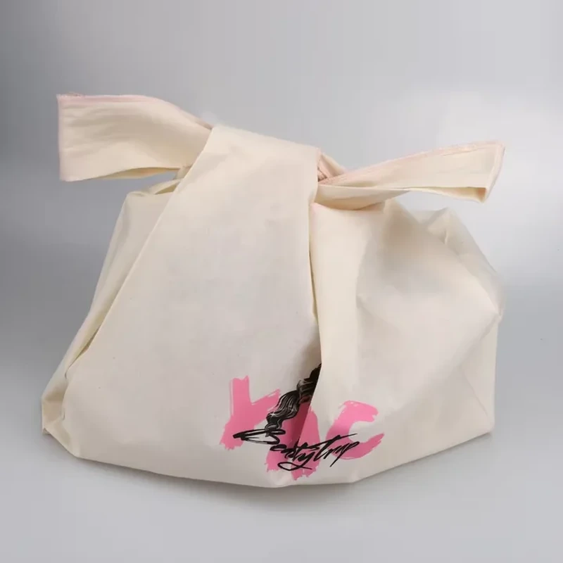 A natural tone bag has broad fabric tie handles and butterfly graphics at the lower corner
