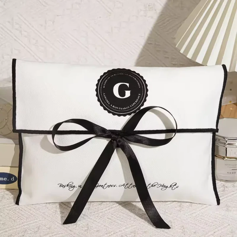 A pale flap pouch uses dark edge piping and a broad ribbon tied across the front