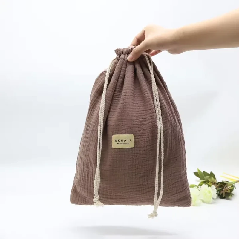 Brown drawstring sack with a crinkled woven texture, cream cords and a small front label.