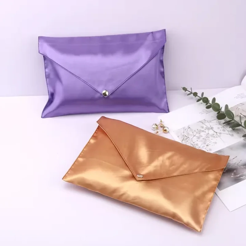 A gently curved satin flap narrows to a central metal snap on a wide envelope