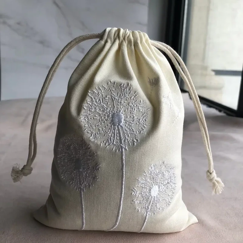 A rounded natural tone pouch shows embroidered dandelion flowers across its lower front
