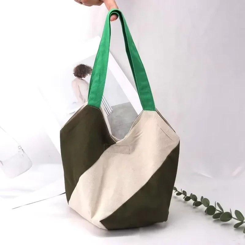 A roomy shoulder tote uses broad diagonal panels and contrasting long green handles