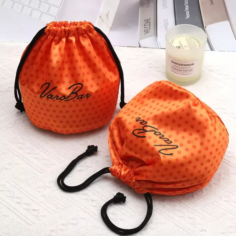 A dotted satin surface, rounded base and dark drawstrings create a short bucket-shaped pouch