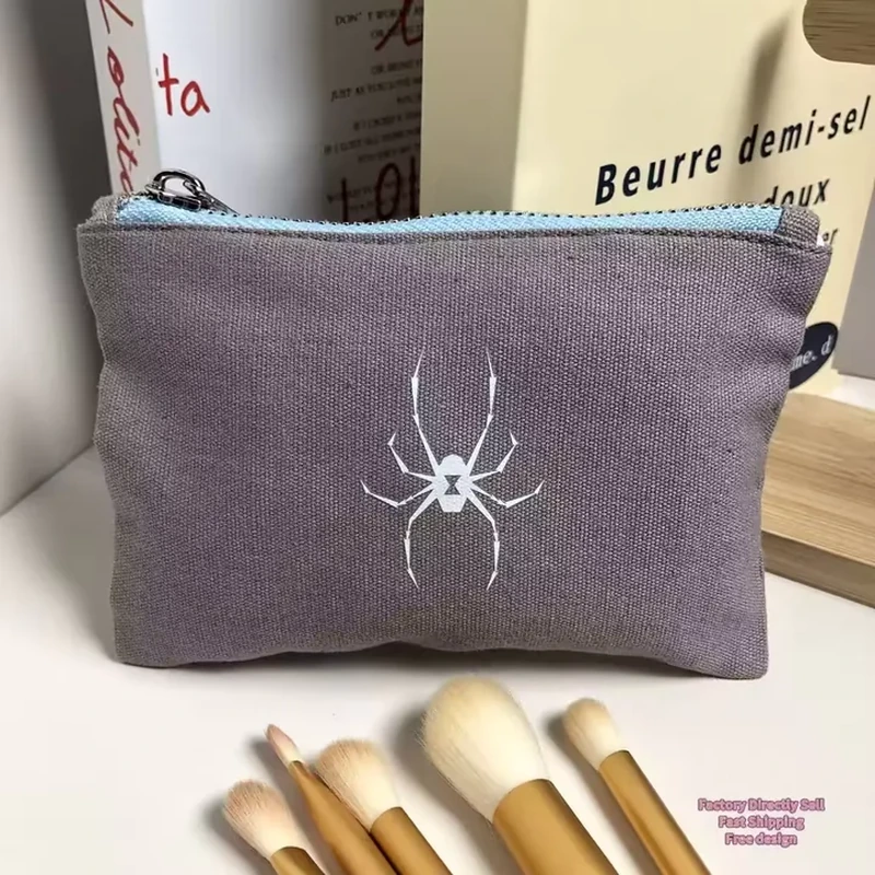 A dark flat pouch has a pale spider motif and a contrasting zipper opening