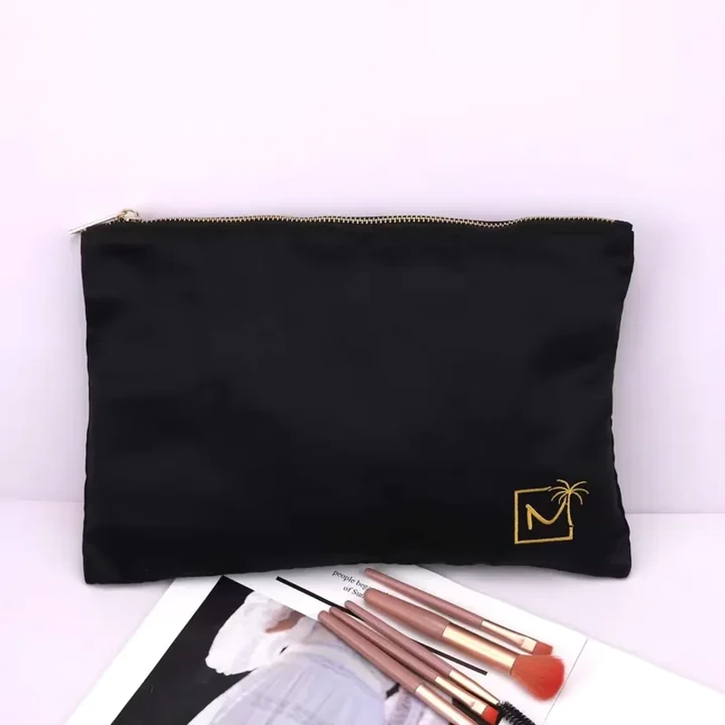 A straight top zipper closes a broad flat satin pouch with a small corner motif