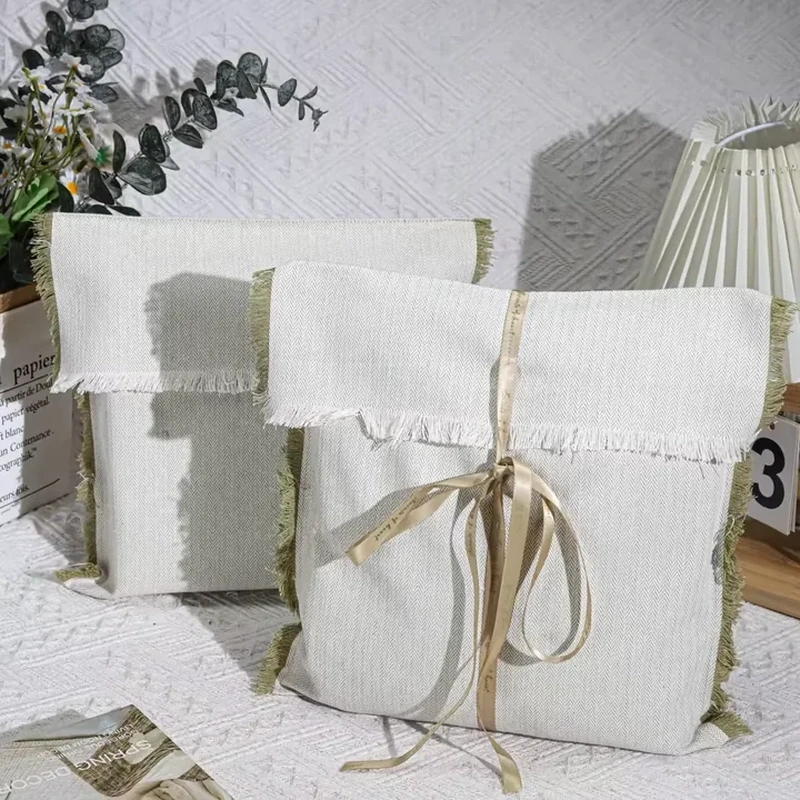 A pale flat pouch features a fringed flap edge and a narrow ribbon tied vertically