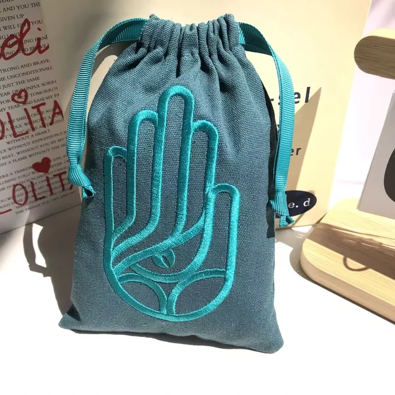 A dark gathered pouch displays a large embroidered hand outline across the front
