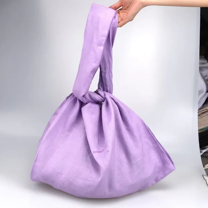 A soft purple bag gathers into a rounded body beneath a distinctive fabric knot handle