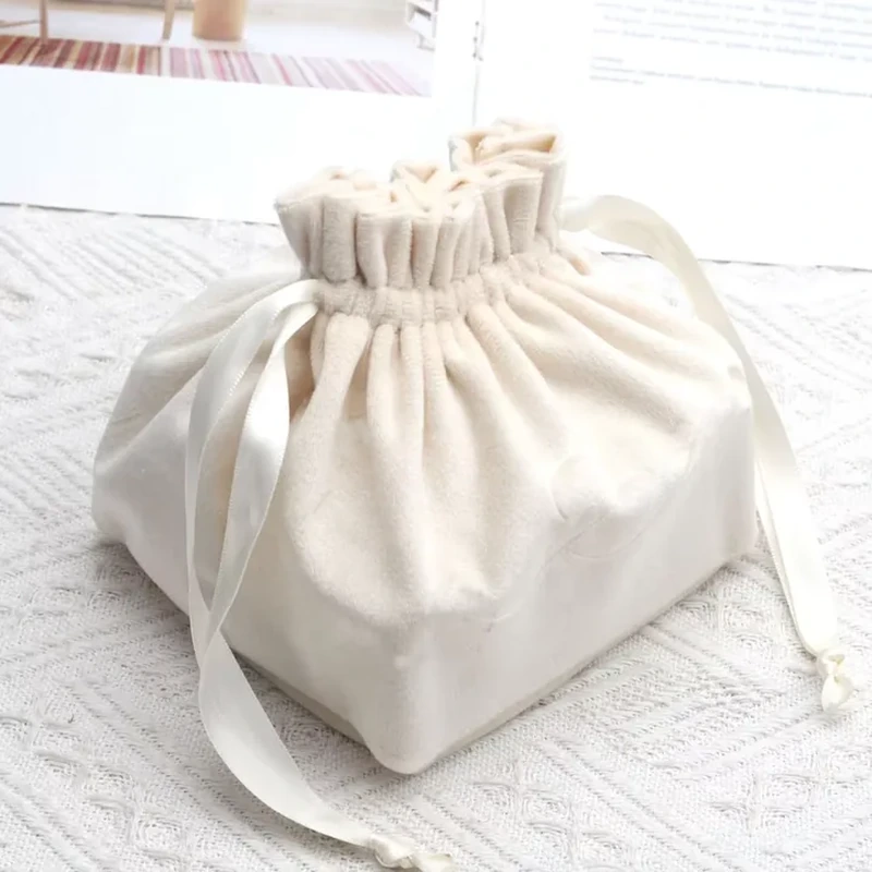 Cream drawstring gift pouch with a rectangular base, ruffled opening and wide ribbon ties.
