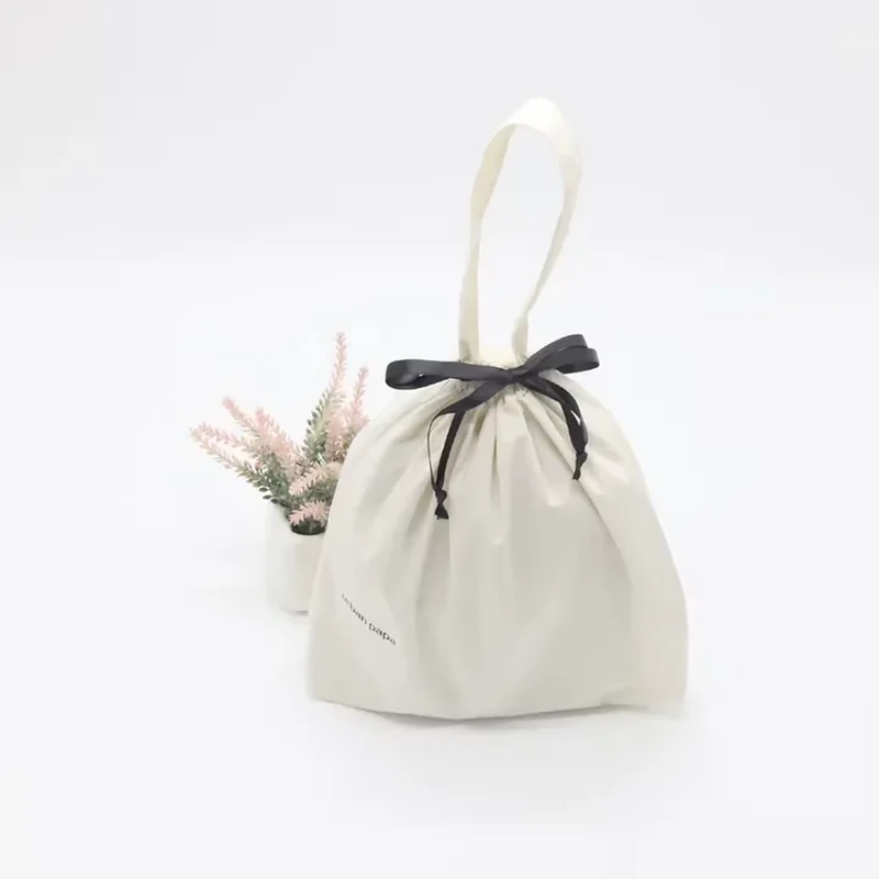 Small ivory gift bag with a single loop handle and a black ribbon bow.