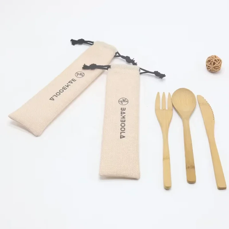 Two narrow cream cutlery sleeves with dark drawstrings beside wooden utensils