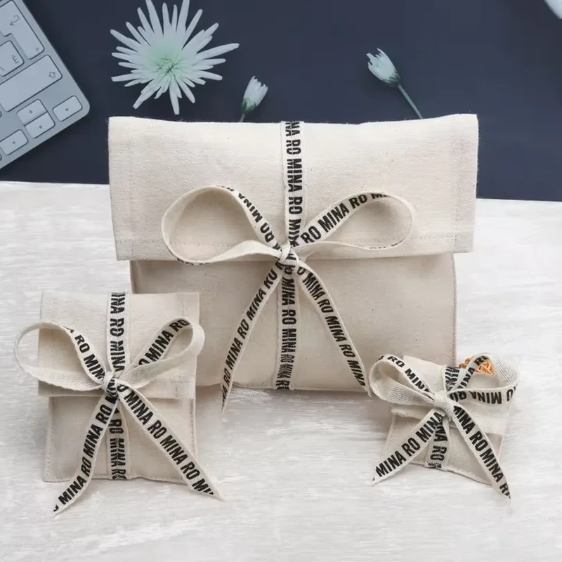 A cream foldover pouch is wrapped with patterned ribbons tied across the front