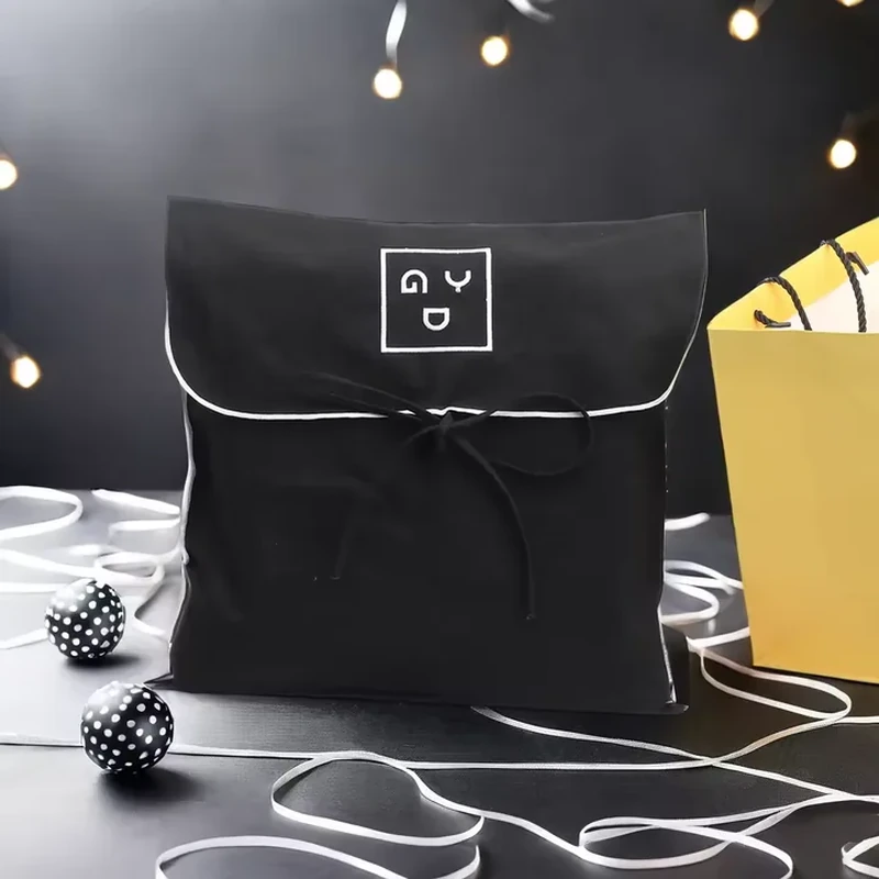 A dark pouch combines a rounded flap, pale edge piping and a narrow front tie