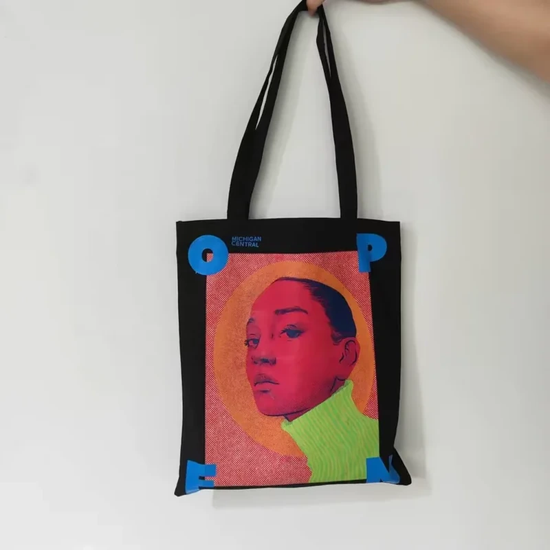 A dark shoulder tote displays a large colorful portrait panel between two long handles