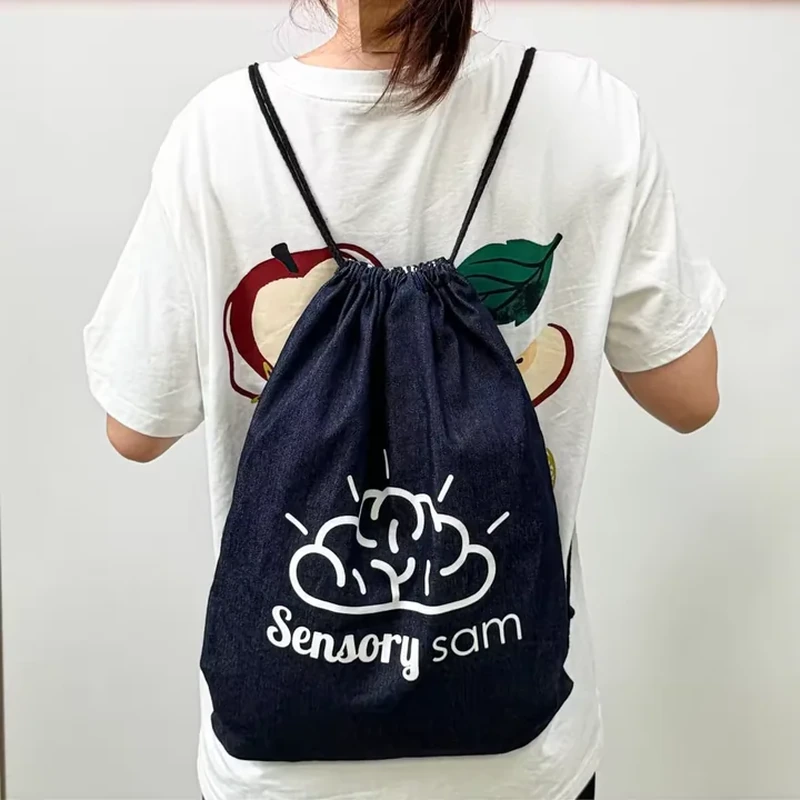 A dark drawstring bag is worn on the back and carries a large pale front illustration