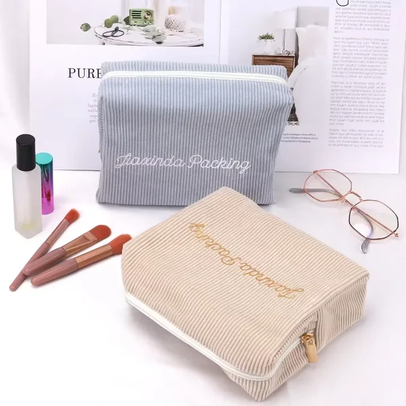 Gray and cream ribbed cosmetic cases with embroidery and zippers running around three edges