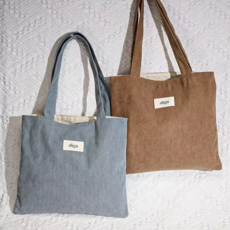 A broad flat tote features vertical ribbing, long handles and a small rectangular label