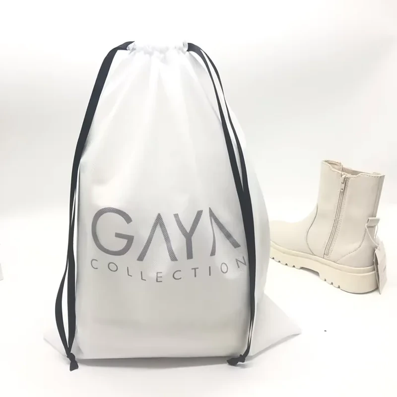 Tall pale shoe bag with black ribbon drawstrings beside a light ankle boot