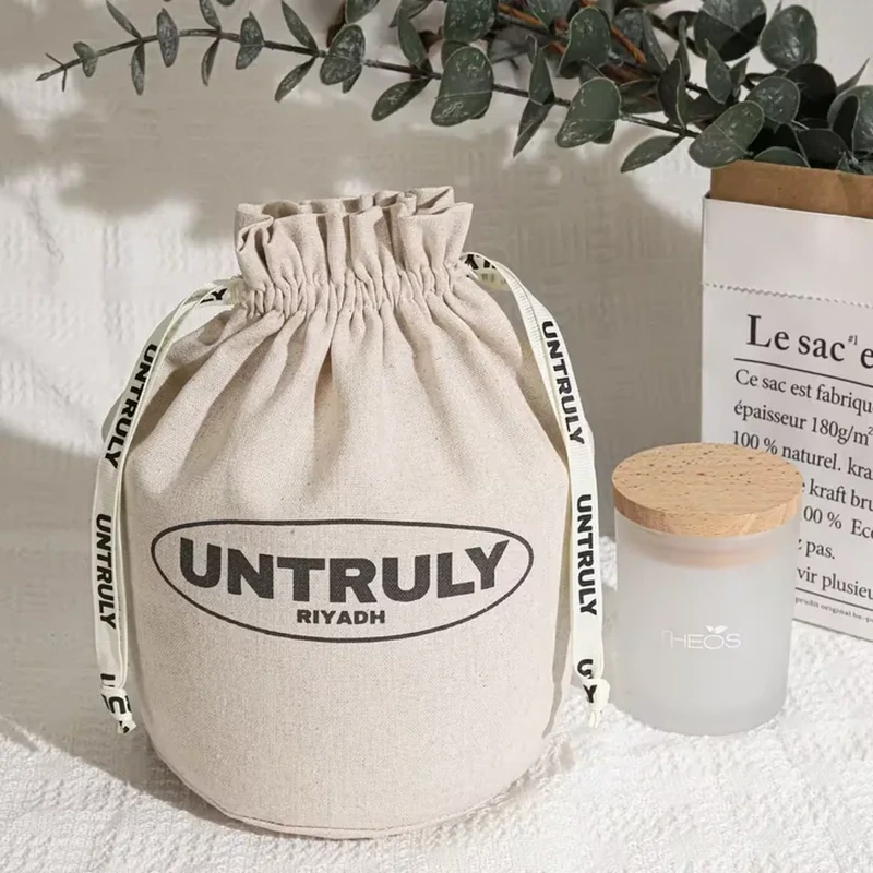 A rounded natural tone pouch has a short gathered neck and a bold framed front label