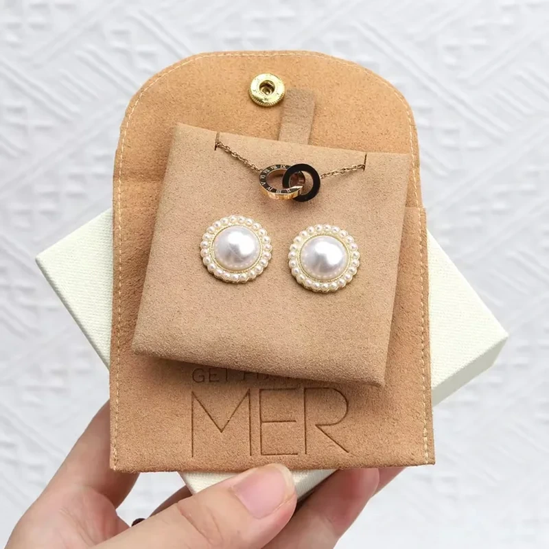 A rounded snap flap opens above a front pocket displaying earrings and a pendant