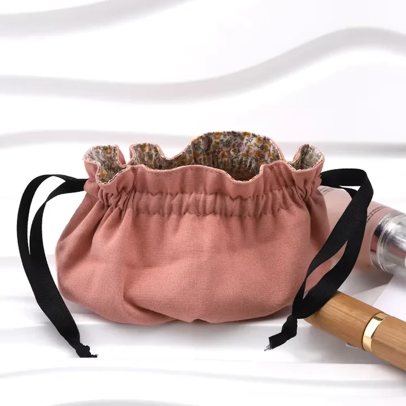 A rounded pouch has a broad gathered opening, a patterned inner edge and dark drawcords
