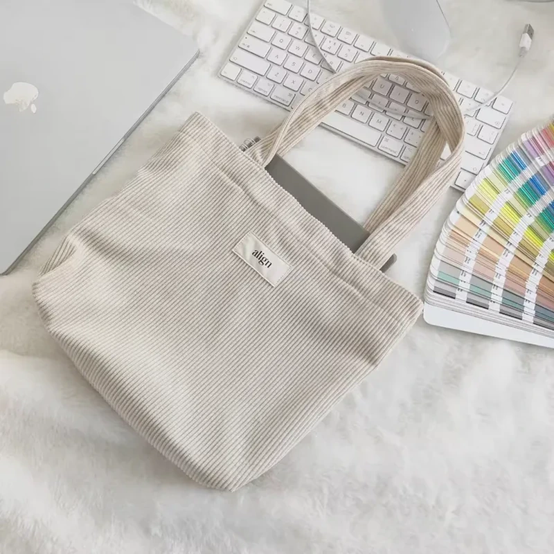 A compact ribbed tote combines short rounded handles with a small sewn front label