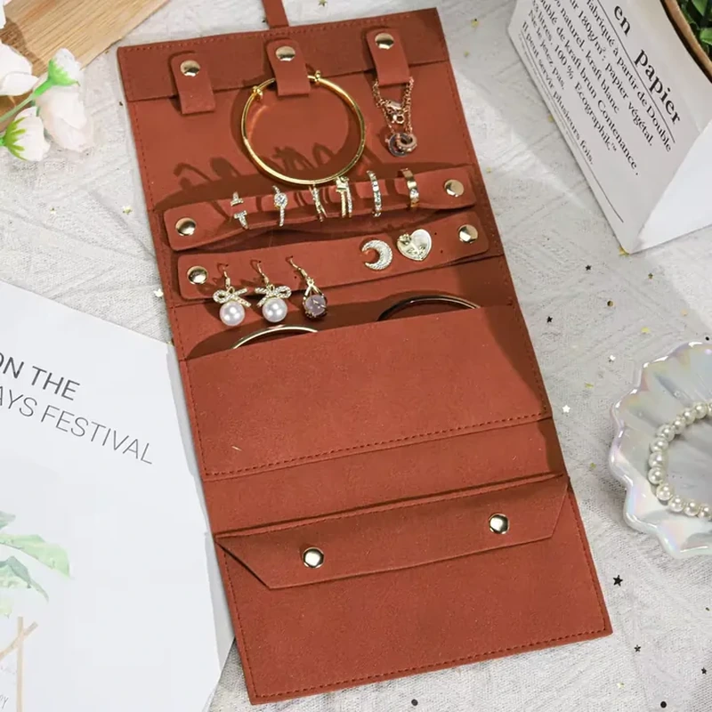 Open terracotta jewelry roll with three upper snap tabs, two horizontal accessory bars and lower storage pockets