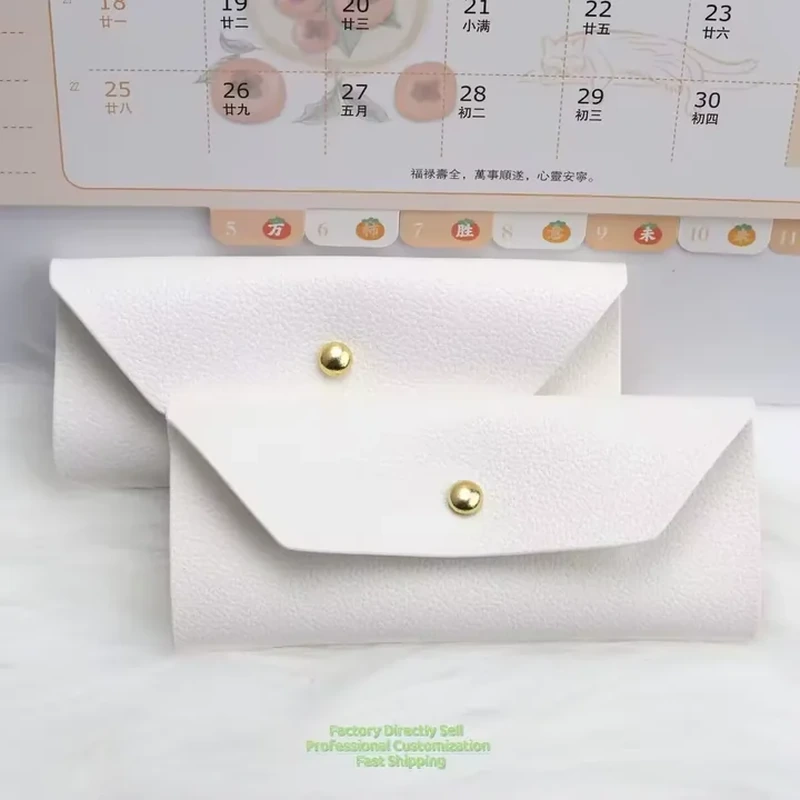 White leather-look envelope pouches with triangular flaps and central gold-colored snaps