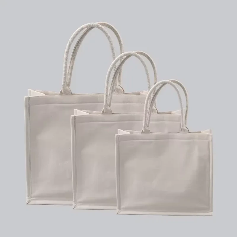 A square pale tote stands upright with rounded handles and visible edge seams