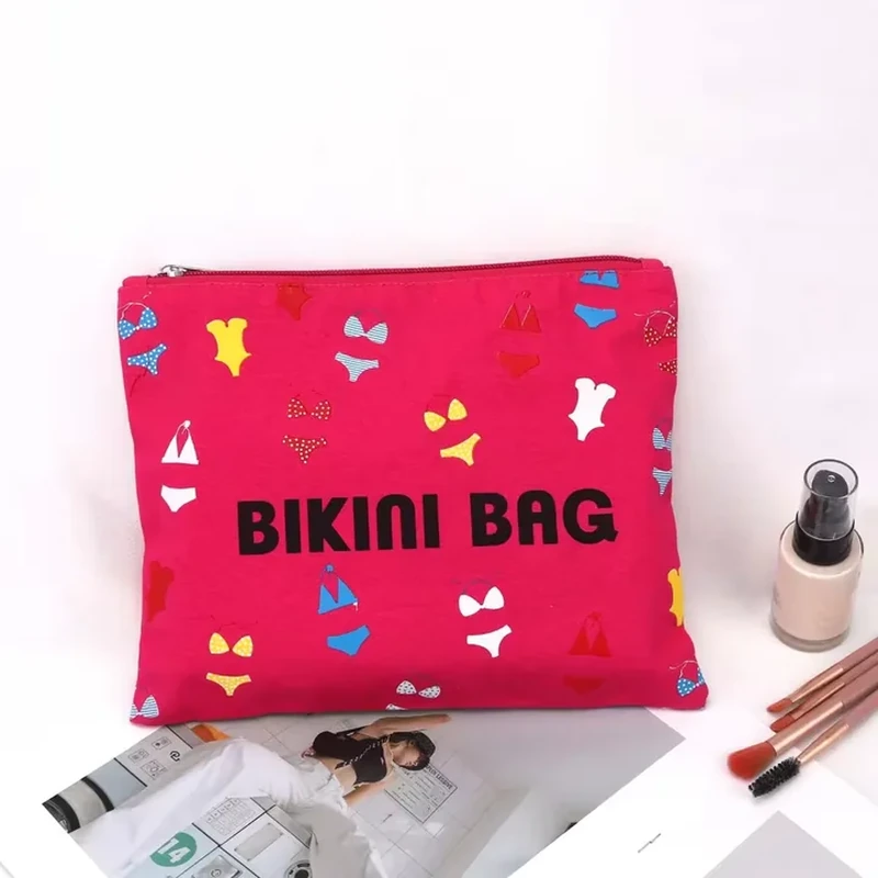 A bright flat zip pouch shows small swimwear motifs around a bold centered front message
