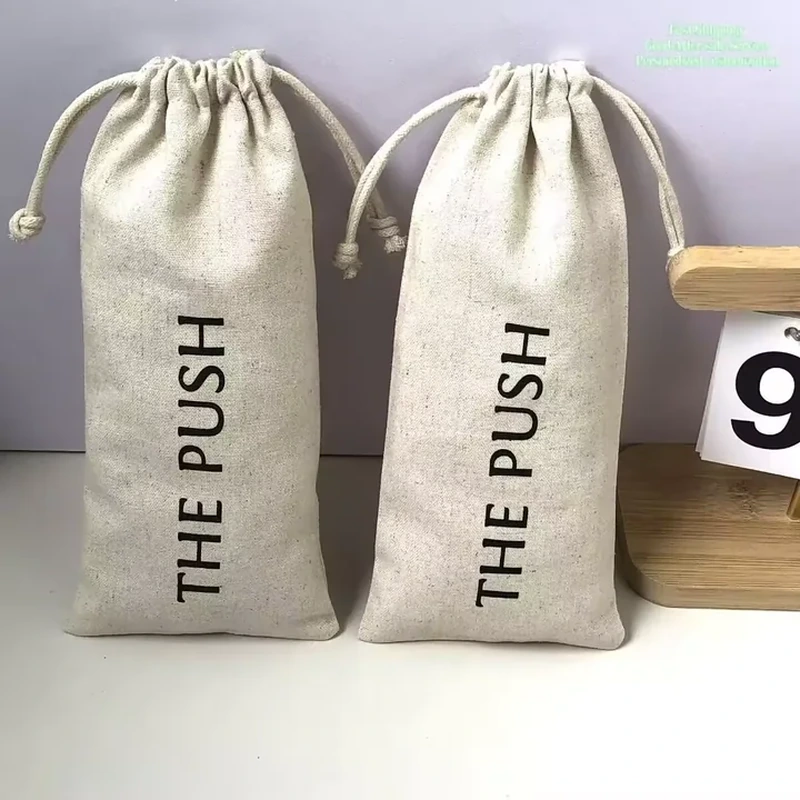Tall pale woven bottle bags with vertical black printing and cream drawstrings