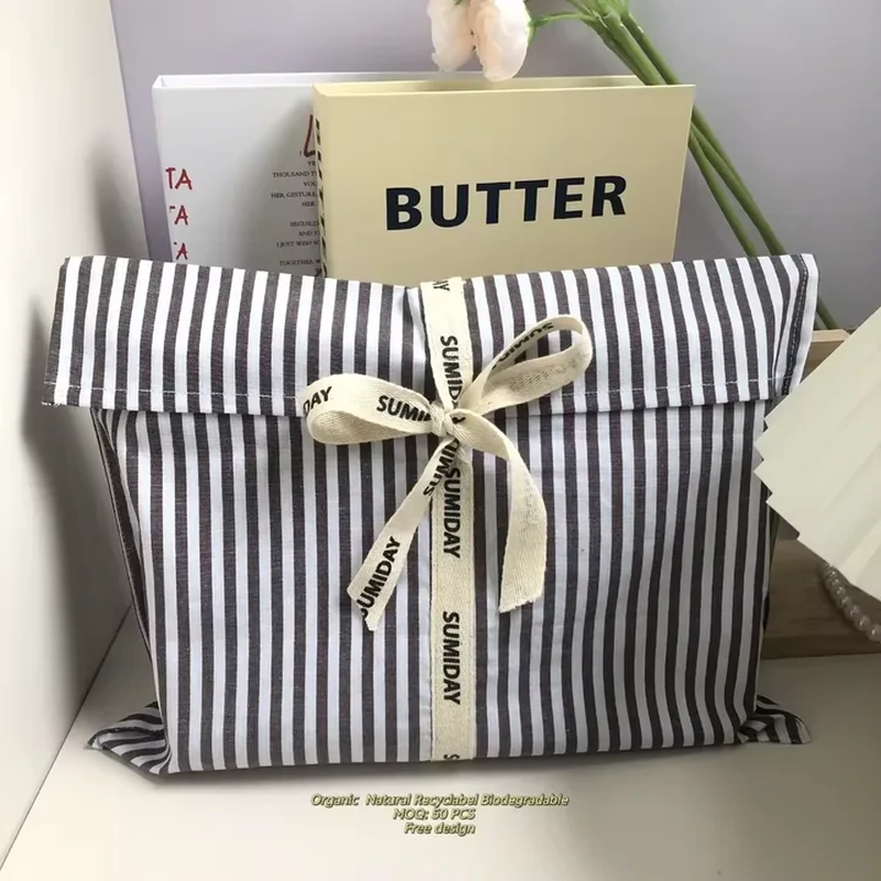 A rectangular gift pouch combines narrow dark stripes with a pale printed ribbon bow