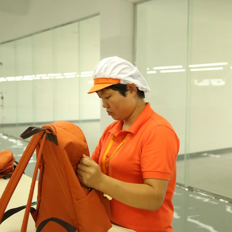 A worker examining the construction of an orange bag at a worktable.