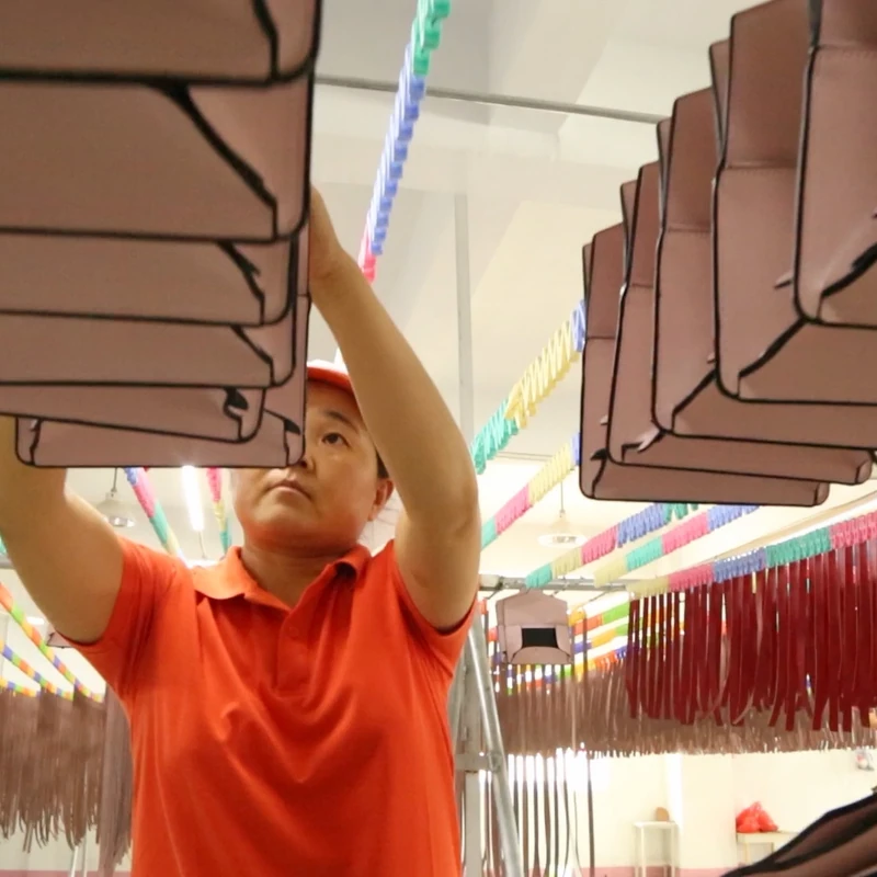 A worker arranging pink bag components on overhead hanging racks.