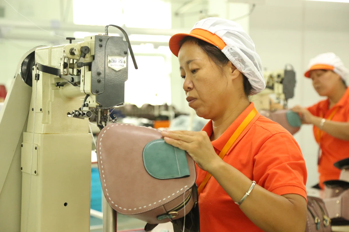An operator stitching the edge of a pink bag at a sewing machine.