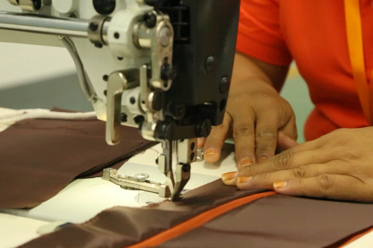 Close-up of an operator stitching a brown bag panel beside an orange zipper.