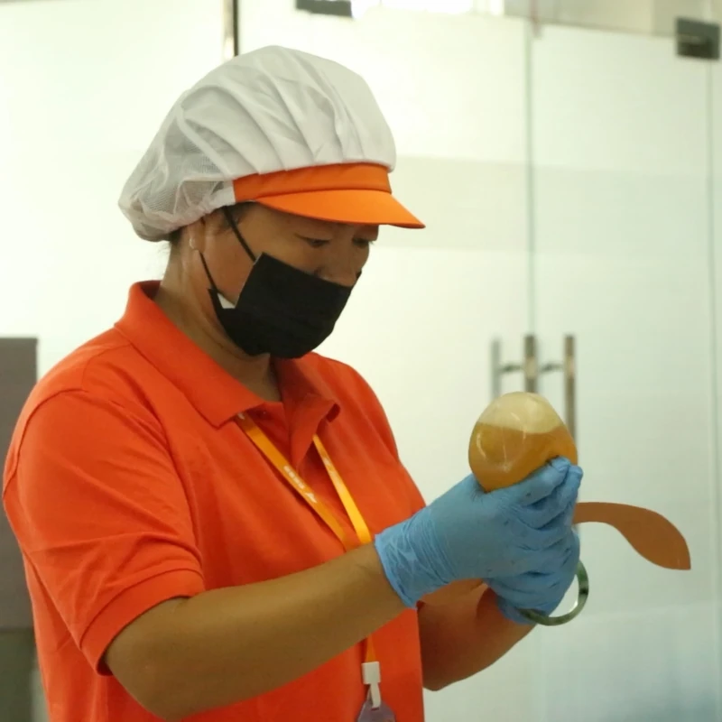 A worker handling a small bag component with a handheld bottle at a worktable.