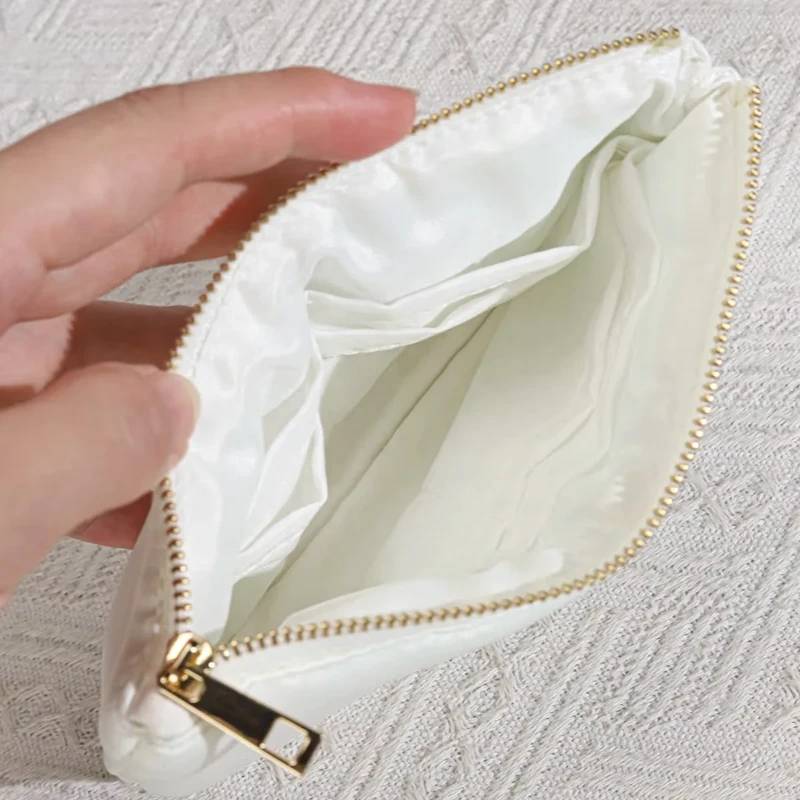 Hand holding open a cream zipper pouch to show its lining