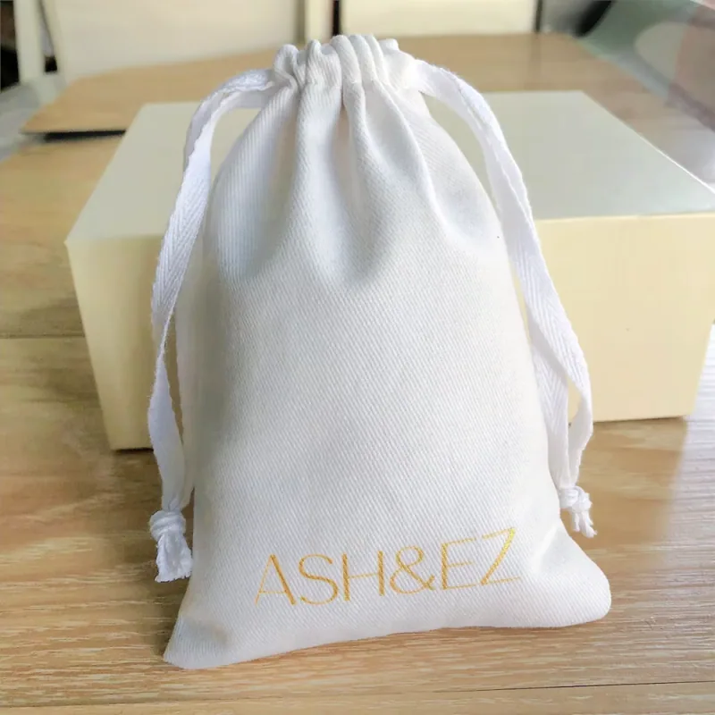 Tall cream drawstring bag with pale cords and a gold printed wordmark.