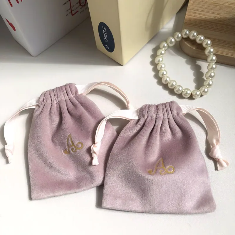 Two soft mauve drawstring pouches beside a pearl bracelet.