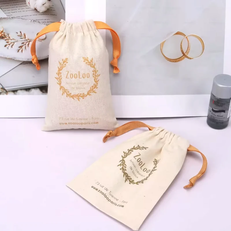 Two cream drawstring pouches with orange ribbon ties.