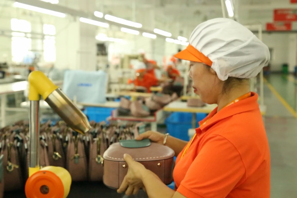An operator holding a small bag at a finishing workstation.
