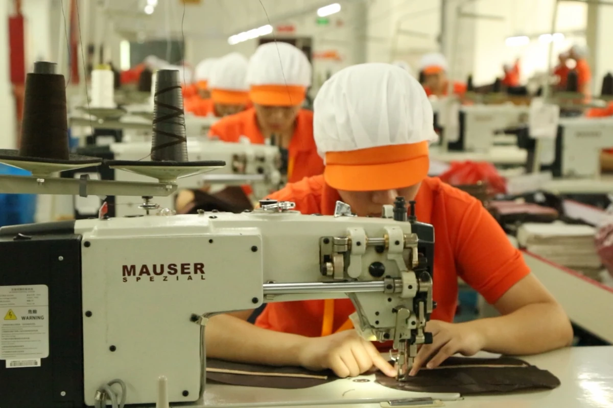 An operator sewing a flat bag panel in a row of industrial workstations.