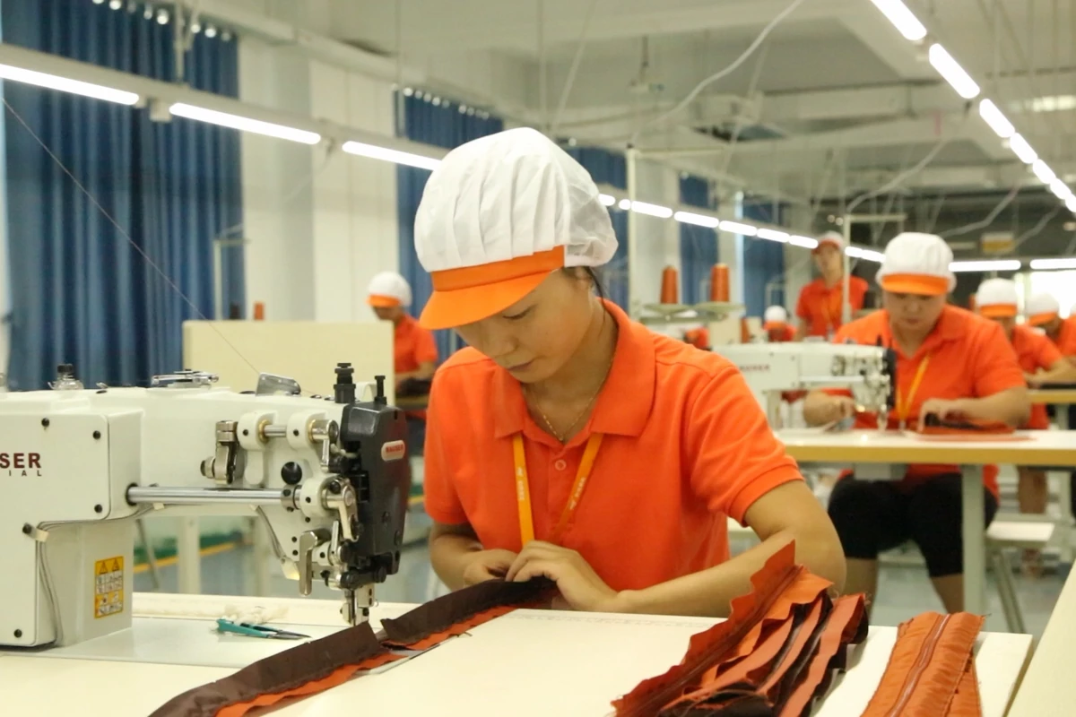 An operator sewing a narrow bag panel beside prepared orange components.