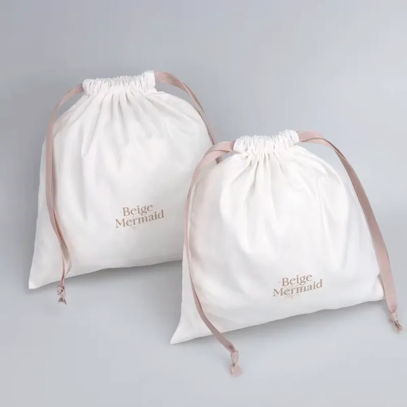 Two white cotton drawstring bags with blush ribbon ties and printed logos