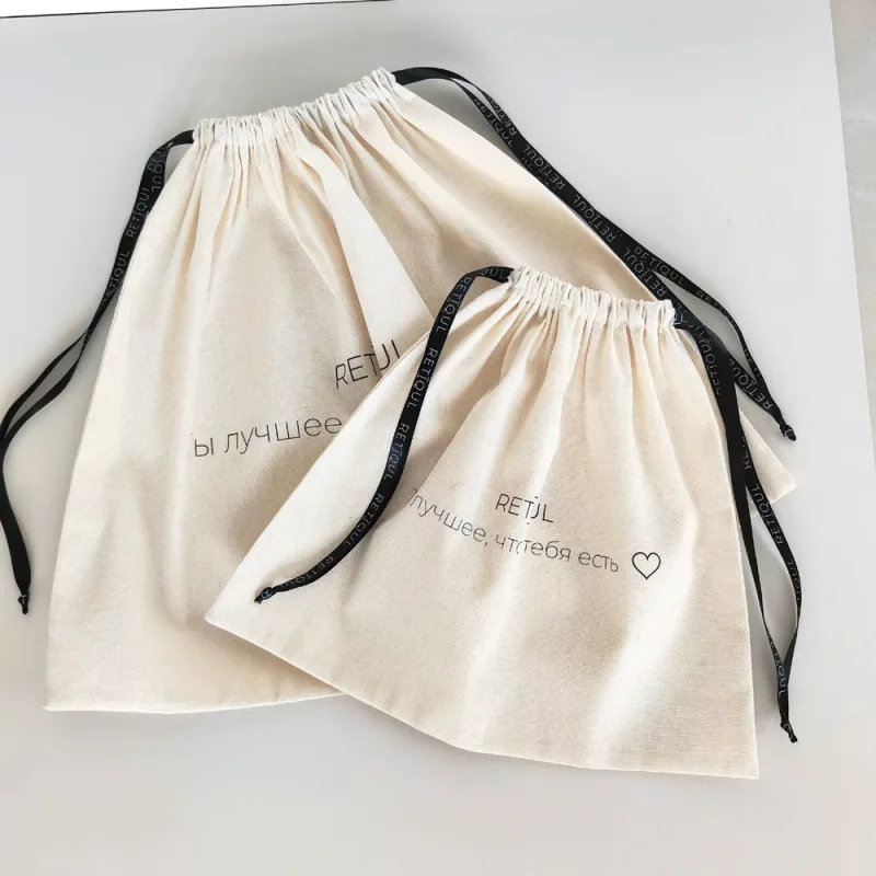 Two natural cotton drawstring dust bags laid flat with black printed ribbon ties