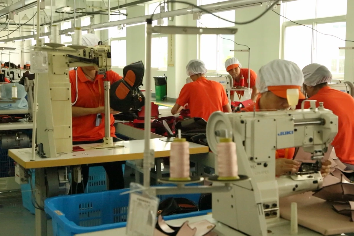 Operators working with bag panels at adjacent sewing workstations.