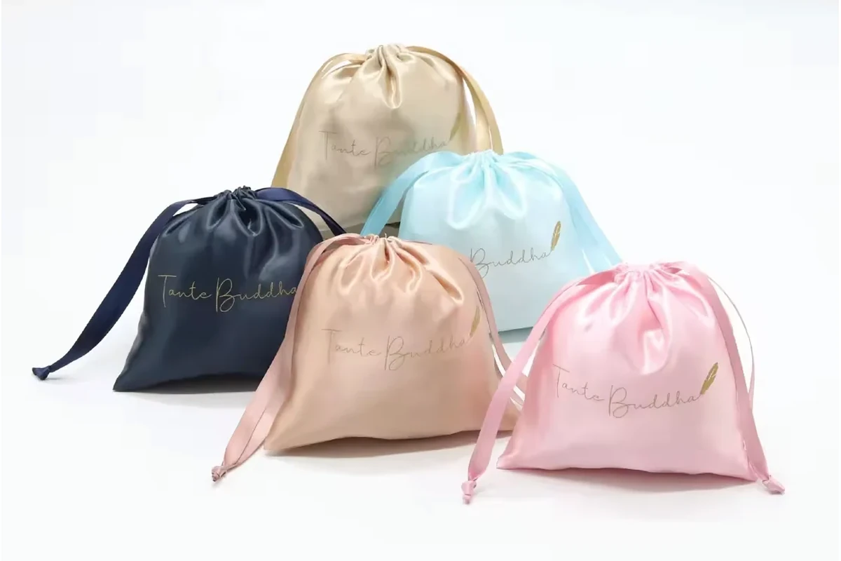 Five satin gift pouches in navy, champagne, pale blue, peach and pink.