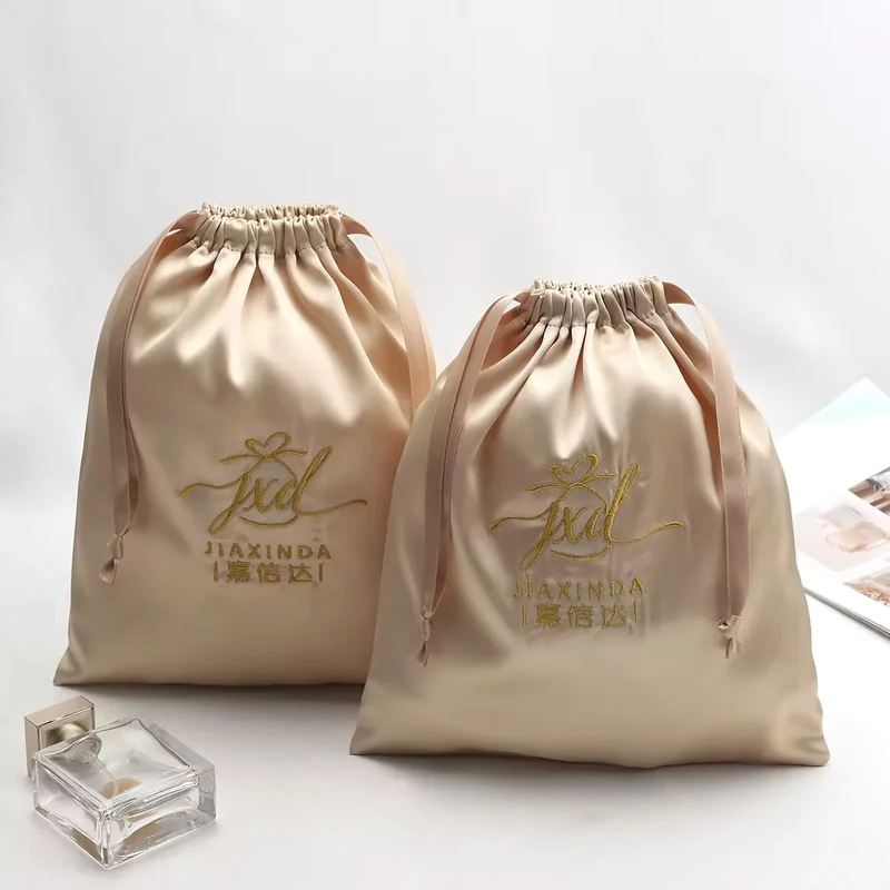 Two champagne satin gift pouches with printed gold logos